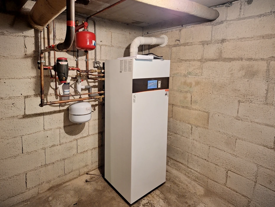 Intérieur d'un local technique avec chaudière murale blanche en cours de maintenance