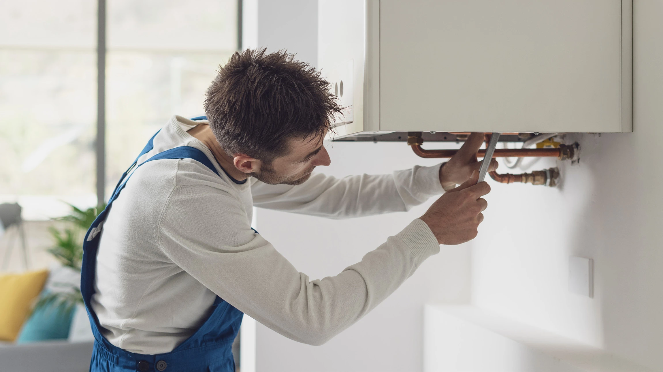 Technicien en combinaison blanche et casque de sécurité effectue la maintenance d'une chaudière murale extérieure