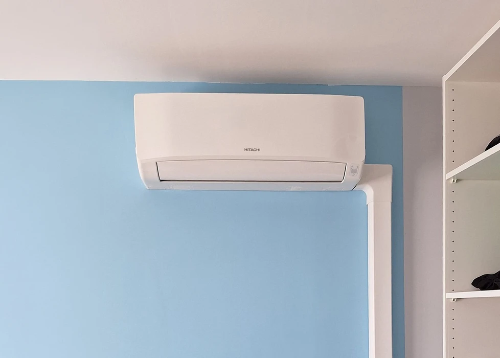 Technicien en combinaison à carreaux et casque rouge effectue la maintenance d'une unité de climatisation extérieure fixée sur mur de briques